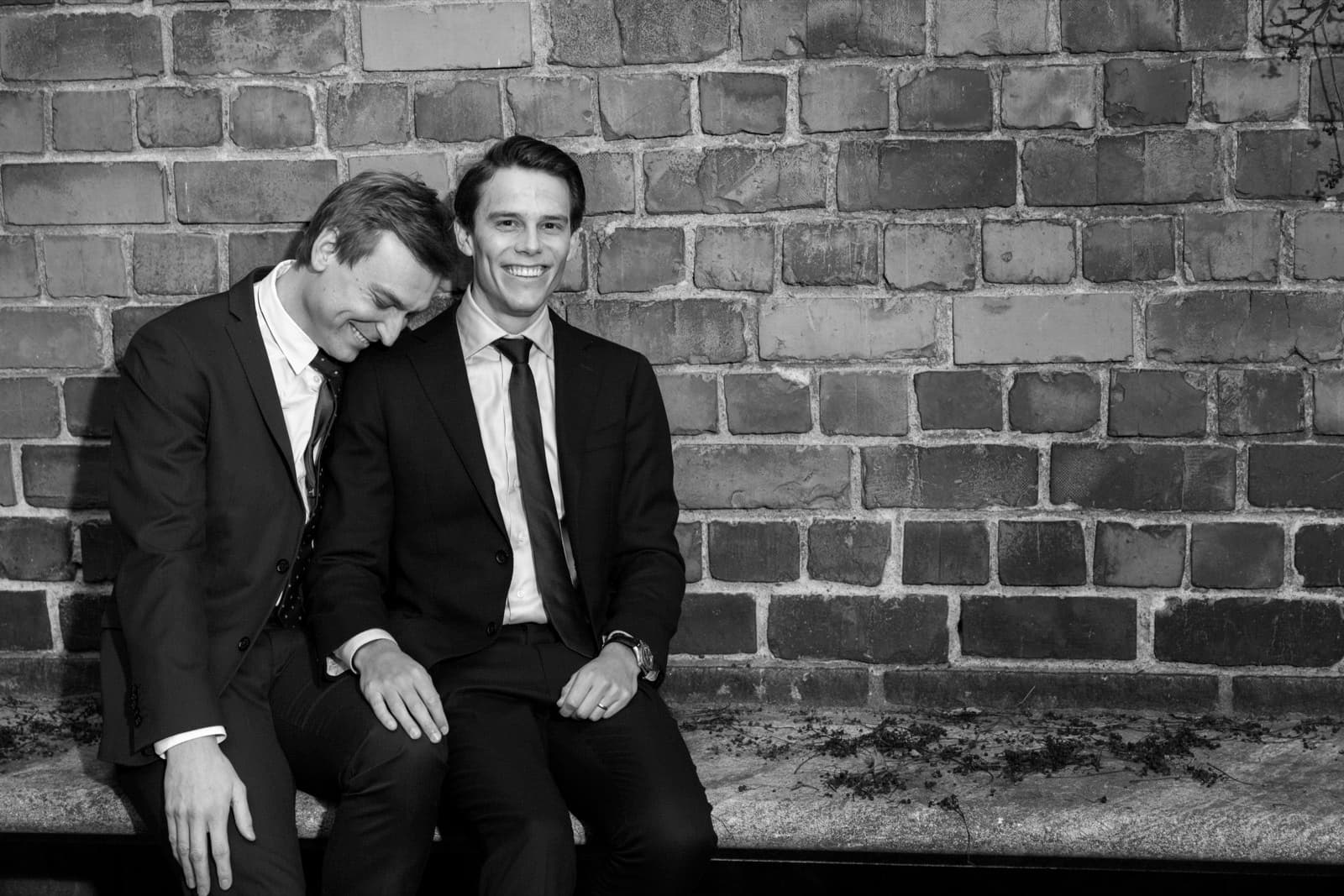 Gustaf and Magnus laughing together on a bench, in black and white